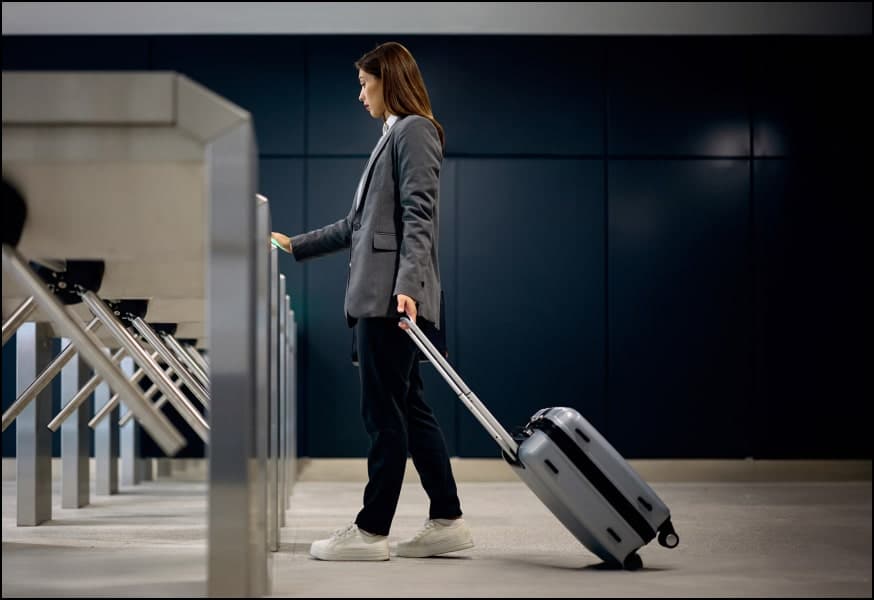 A woman with a roll behind suitcase standing at a security gate