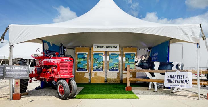 A tent at the state fair, hosting the Harvest of Innovations exhibit, featuring a tractor and a cow statue.